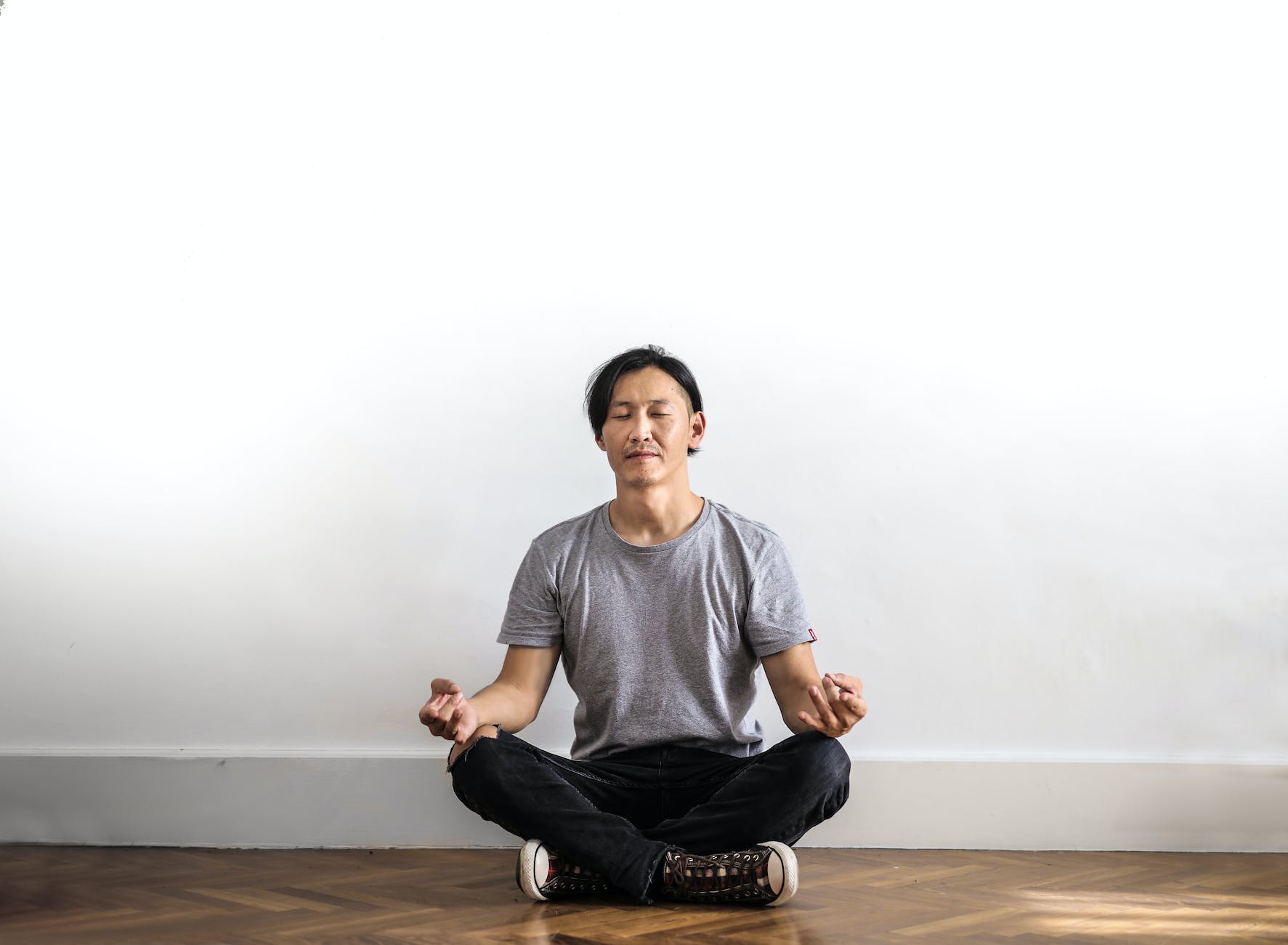 photo of man in gray t shirt and black jeans on sitting on wooden floor meditating